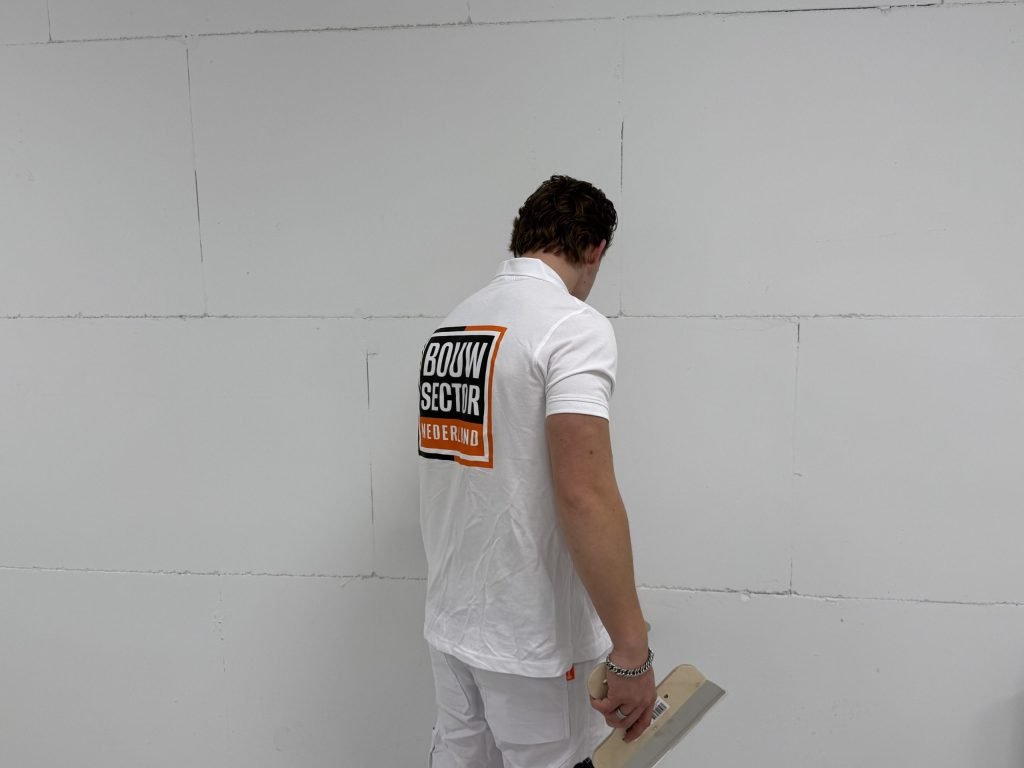 Stukadoor met een spaan in de hand bekijkt een wand van grote witte platen voordat hij begint