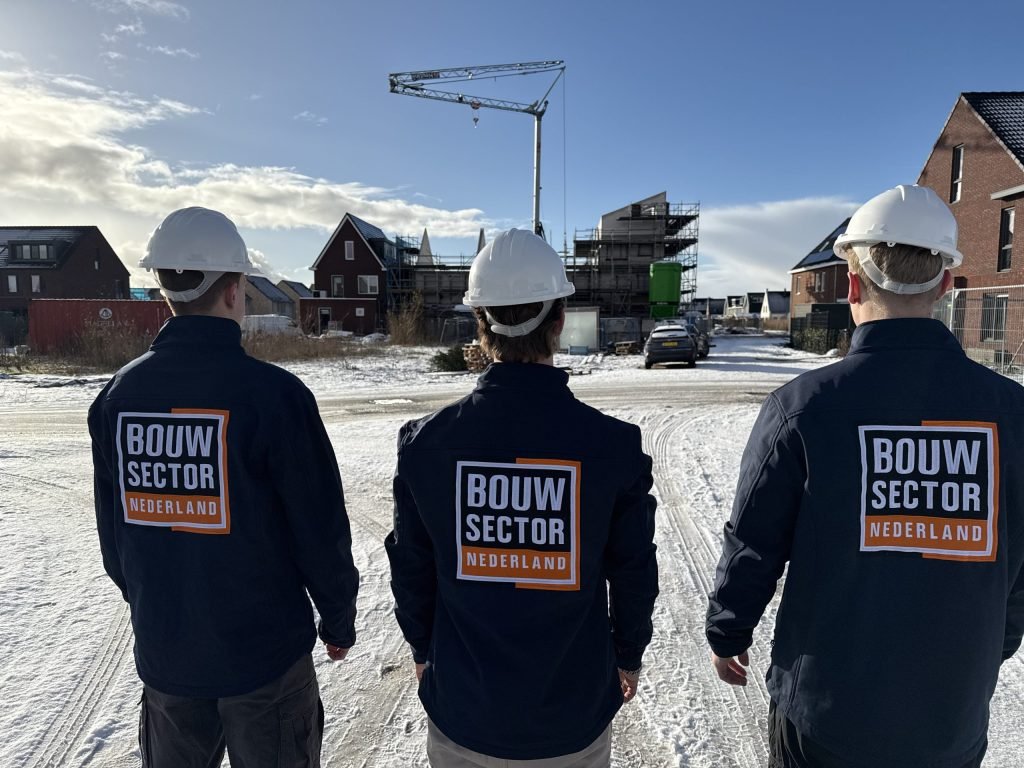 Drie mannen in jassen van Bouwsector Nederland bekijken de bakstenen gevels van een straat met nieuwe huizen