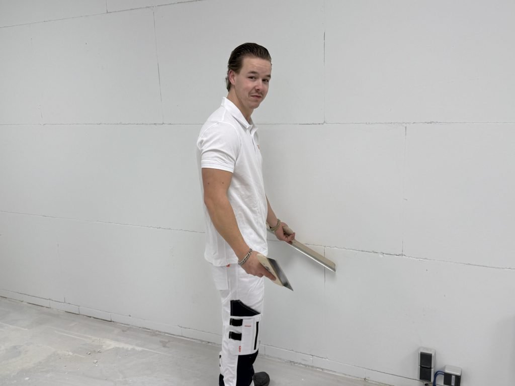 Stukadoor van Bouwsector Nederland met spaan en plakspaan voor een kale wand met naden kijkt om