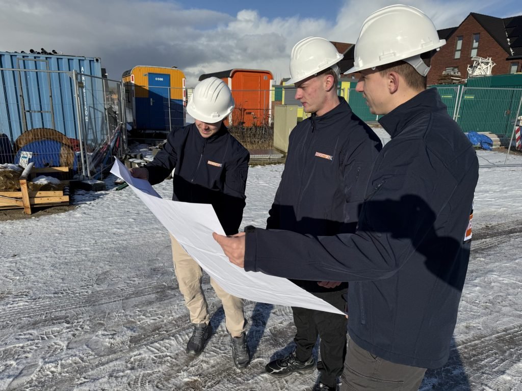 Vakmensen van Bouwsector Nederland met witte helmen bekijken een bouwtekening tussen bouwmaterialen